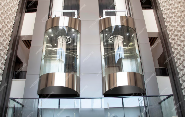 Two glass elevators with stainless steel frames inside a modern multi-story building.