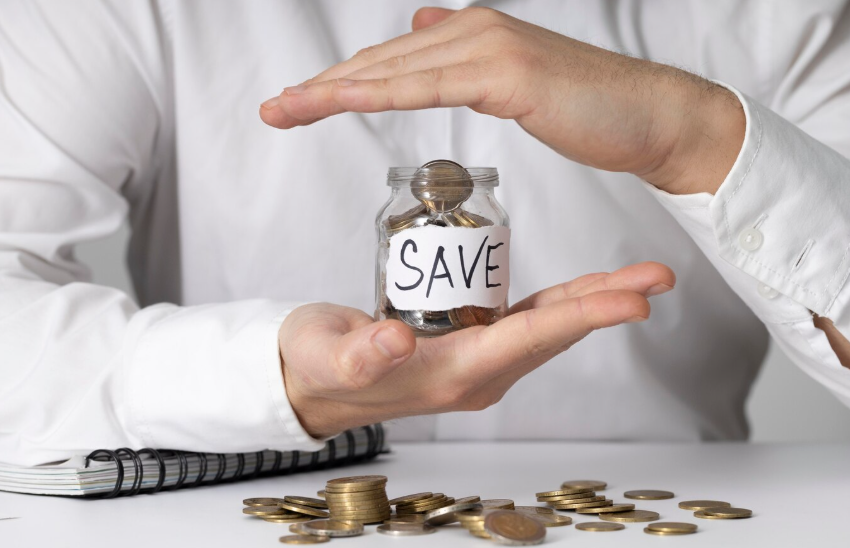 Person holding a small glass jar labeled "SAVE" filled with coins.