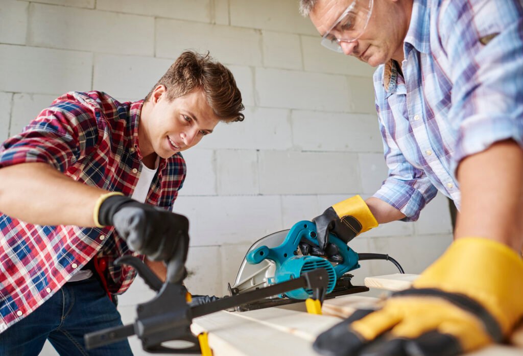 Person building a wall with bricks and mortar alongside a professional mason working on a wall.