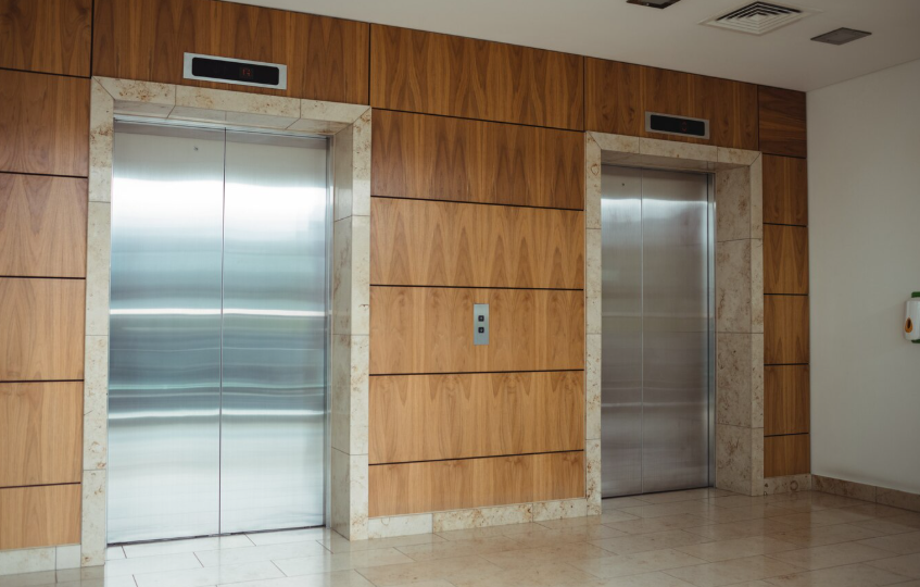 Two stainless steel elevators in a modern lobby with wood and marble wall paneling.